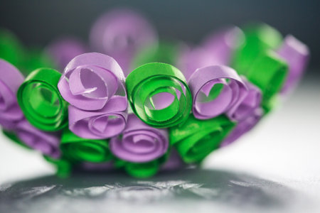 A close-up of a decorative bowl crafted from intricately rolled purple and green paper strips,...