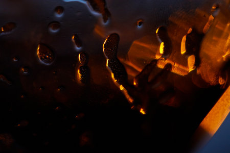 Close-up shot showcasing molten-looking reflections and warm orange highlights. Abstract Amber-Glow Macro of Glassy Surface and Droplets.の写真素材