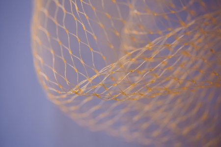 Abstract macro of a golden nylon net against a soft purple background. Flowing synthetic fibers with...