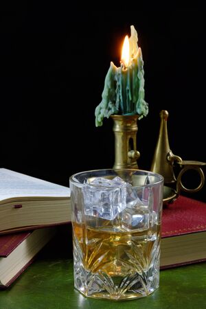 A glass of whisky with ice standing on an antique book, with candle - text in book not subject to copyrightの写真素材