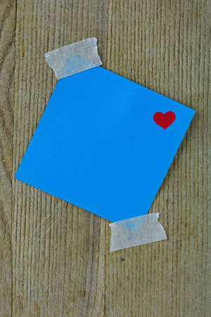 Blue post it note with heart taped to a wooden backgroundの写真素材