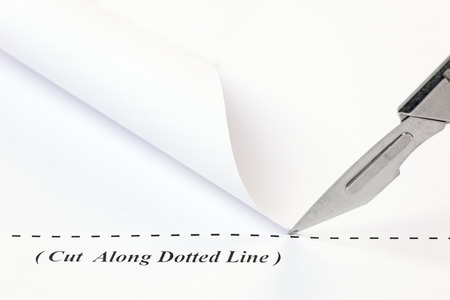 Close up of a scalpel cutting along a dotted line on a sheet of white paper.の写真素材