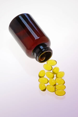 Vitamin capsules spilling from a bottle on to a purple surfaceの写真素材