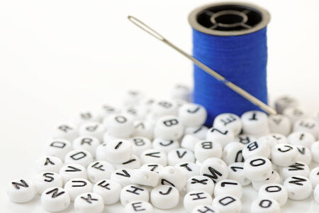 Close up of a pile of letter beads with a reel of cotton and a needle. Shallow depth of field