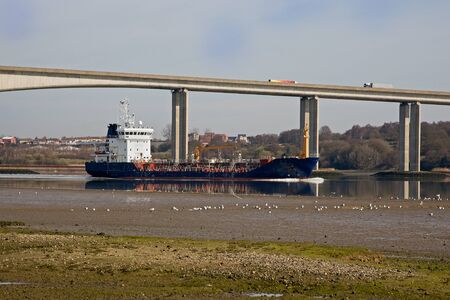 A ship carrying gas passing under a motorway bridge at low tide in the UKの写真素材