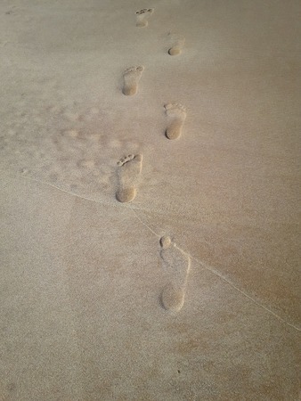 Woman walking on sand beach leaving footprints in the sand. Closeup detail of female feet.の写真素材