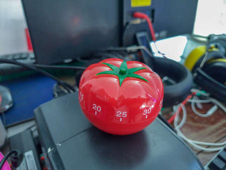Pomodoro kitchen timer in form of a red tomato laying on a wooden table , with colorful objects...