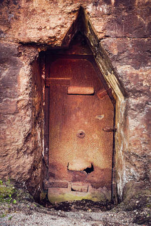 Old thick stone wall with rusty metal doorの写真素材
