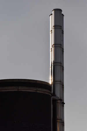 A metal industrial chimney with the setting sun shining on itの写真素材