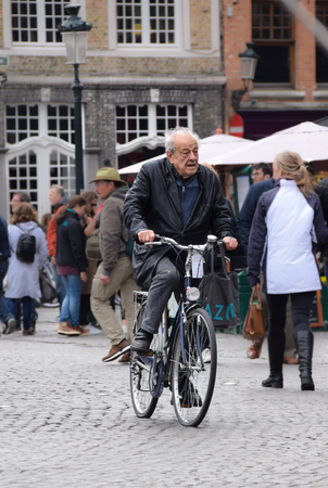 Bruges, Belgium - April 28 2018:   A candid photo of an elderly gentleman rides his Bike through Markt squareのeditorial素材