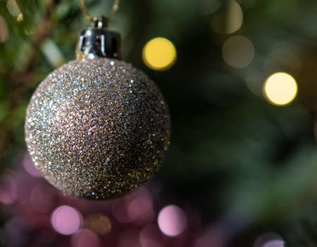 A glittery Bauble hanging on a Christmas tree with the tree and lights behind out of focusの写真素材