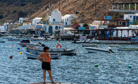 Ormos Korfou, Greece - July 16 2019:   A tourists looks over the boats and cafes around  the harbour of windmill and cafeのeditorial素材