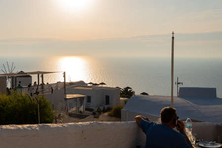 Oia, Greece - July 16 2019:   A diner admires the sunset in a restaurant in the centre of Oia overlooking the Aegean Seaのeditorial素材