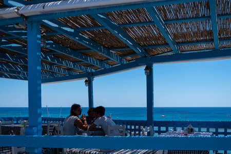 Perissa, Greece - July 18 2019:   Diners at a sea view restaurant overlooking the waters of the Aegean on the Perissa sea front roadのeditorial素材