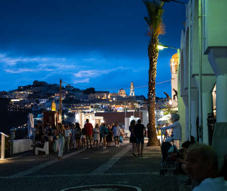 Fira, Greece - July 14 2019:   Night time shot of Tourists walking along the cliff top road of Ipapantisのeditorial素材