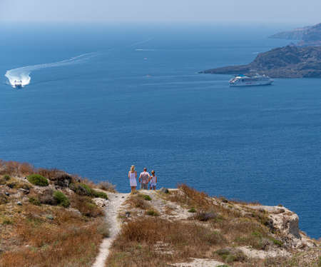 Megalochori, Greece - July 17 2019:   A family of tourists admiring the view of the Aegean Sea as they walk along Santorini's cliff top path over the headland near Megalochoriのeditorial素材