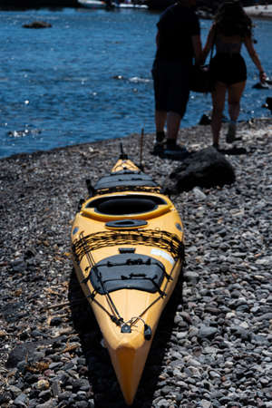 Akrotiri, Greece - July 19 2019:   A yellow canoe points past two holiday makers towards the Aegean Sea on Akrotiri beachのeditorial素材