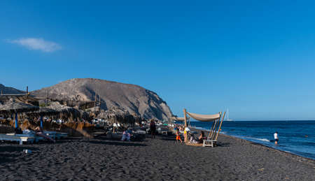 Perissa, Greece - July 11 2019:   The view of holidaymakers, sun loungers and parasols along the sea shore of Perissa Beachのeditorial素材
