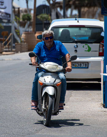 Perissa, Greece - July 11 2019:   A man in sunglasses riding a scooter along the Perivolos Sea front roadのeditorial素材
