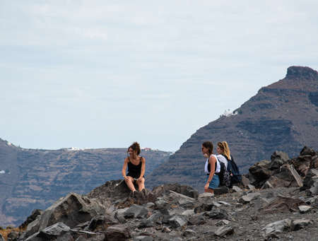 Nea Kameni Island, Greece - July 16 2019:   Three holidaymakers admire the view from a rest stop part way up the Volcanic mountain of Nea Kameniのeditorial素材
