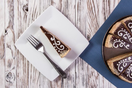 Cake covered with chocolate on a wooden table. A piece of cake in a plateの写真素材