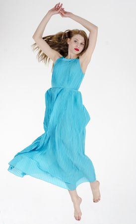 Young slender long-legged girl with a fashionable hairstyle and wearing a blue creme dress dancingの写真素材