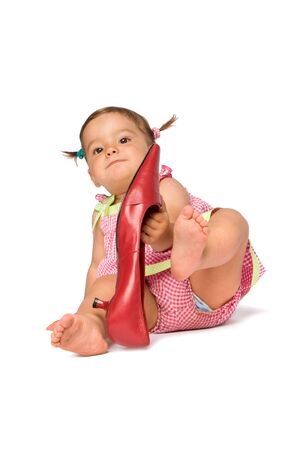One year old baby girl try on big red shoe, isolated on white background.の写真素材