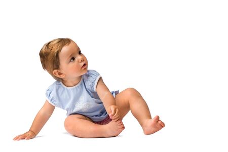 Baby girl sitting on the ground and looking at something with interest, isolated on white background.の写真素材