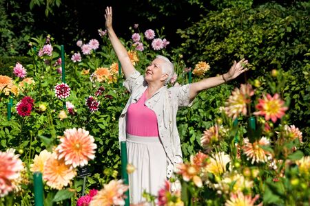 Happy senior woman expressing positivity in the garden full of flowers.の写真素材