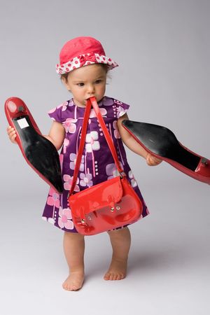 Funny shot of one year old fashion girl with red purse and big adult shoes.の写真素材