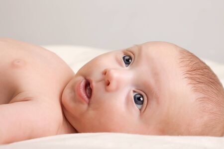 Ten weeks old cute little baby girl with curious look on her face lying comfortably on bed