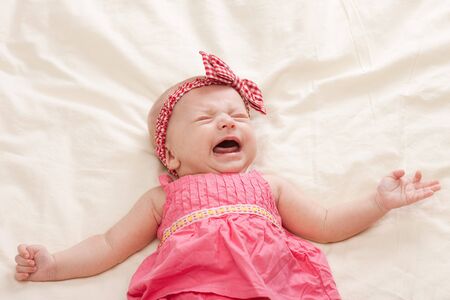 Crying and gesturing ten weeks old baby girl on bedの写真素材