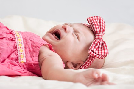 Crying ten weeks old baby girl on bedの写真素材