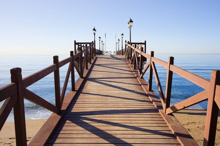Wooden pier in good condition with barriers and lanterns on a calm Mediterranean Sea in Marbella, Costa del Sol, Andalusia, Spain.の写真素材