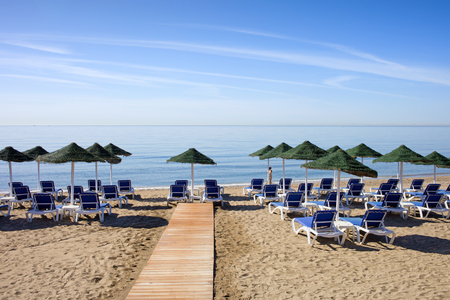 Sun loungers with umbrellas on a sandy beach by the Mediterranean Sea at the popular resort of Marbella in Spain,  Costa del Sol, Andalusia, Malaga province.の写真素材