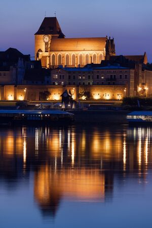 Old Town of Torun in Poland, reflection on Vistula River waters, illuminated Cathedral Basilica of...