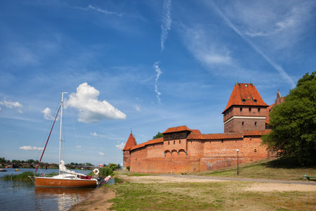Malbork Castle in Poland, sailboat moored at Nogat River shore, medieval fortress of the Teuronic...
