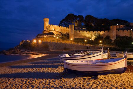 Tossa de Mar at night, seaside town on Costa Brava in Catalonia, Spain, medieval wall of the Old Town (Vila Vella), fishing boats on a beachの写真素材