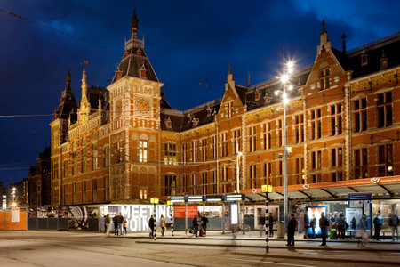 Amsterdam, Holland, Netherlands - May 10, 2013: Amsterdam Central Train Station and tram stop at night, illuminated Gothic and Renaissance Revival style facade, city landmark.のeditorial素材