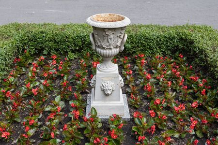 Pedestal for flowers, plants with classic style ornate vase in red flowers flowerbed with hedge, Saxon Garden, public park in Warsaw, Poland.の写真素材