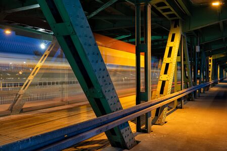 Bridge by night with tram light trails behind metal frame in Warsaw, Poland.
