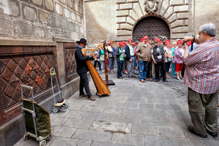 Barcelona, Spain - May 18, 2014: Group of tourists listen to basker playing harp, street musician in...