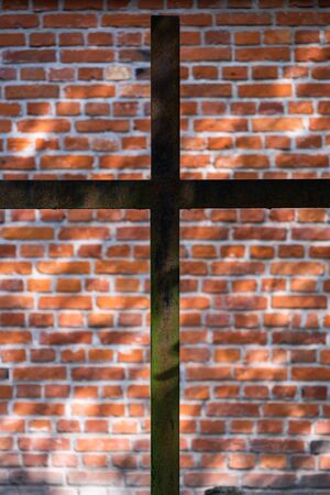 Simple metal Christian cross contrasting against brick wall, symbol of Christianity, shallow depth of field.の写真素材