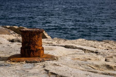 An old rusty mooring bollard at sea waterfront in Malta, shallow depth of field.