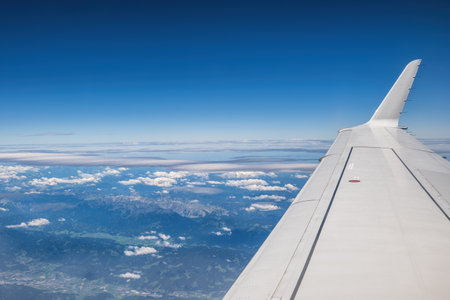 Sky with cumulus and cirrus clouds, airplane wing and mountains below, aerial view above Slovenia.の写真素材