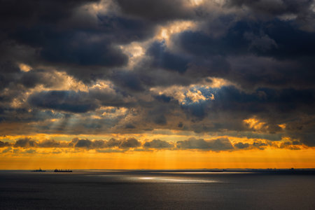 Cloudscape over the Baltic Sea with sun shining through rain clouds and spotlight reflection in water, northern Poland.の写真素材