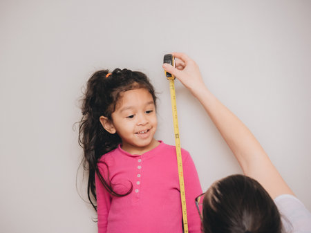 young millennial mother at home measuring daughter with tape measureの写真素材