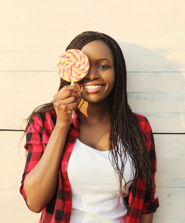 Portrait beautiful happy smiling african woman having fun with sweet lollipopの写真素材