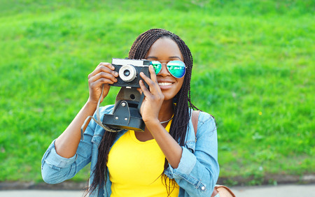 Portrait happy smiling african woman with retro vintage camera in city parkの写真素材