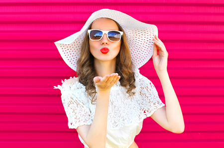 Woman in summer straw hat sends an air kiss over colorful pink backgroundの写真素材